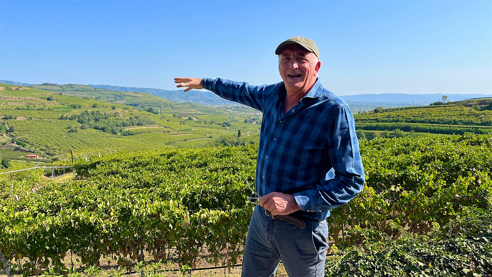 Graziano Prà standing on a hillside pointing out at the vineyards below